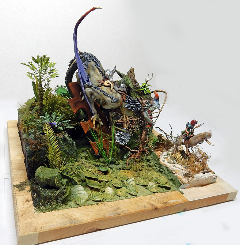 Diorama de maquettisme montrant un dragon bleu et un cavalier dans un décor végétal luxuriant