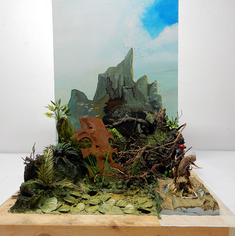 Diorama de maquettisme avec montagne peinte, végétation luxuriante et figurine de cavalier chevauchant une créature dragon