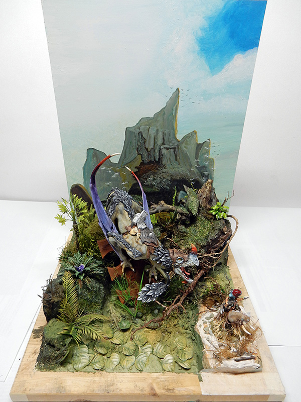 Diorama de maquettisme avec dragon ailé aux écailles grises dans un paysage montagneux végétalisé