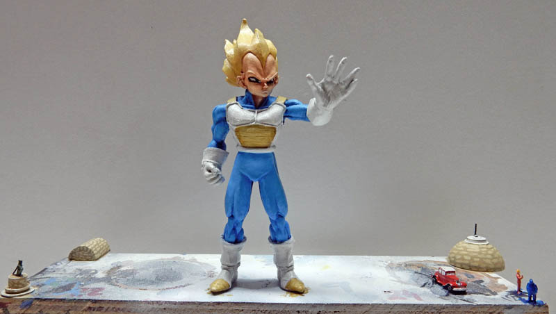 Figurine de Vegeta Super Saiyan paume tendue sur un diorama avec maisons et personnages miniatures