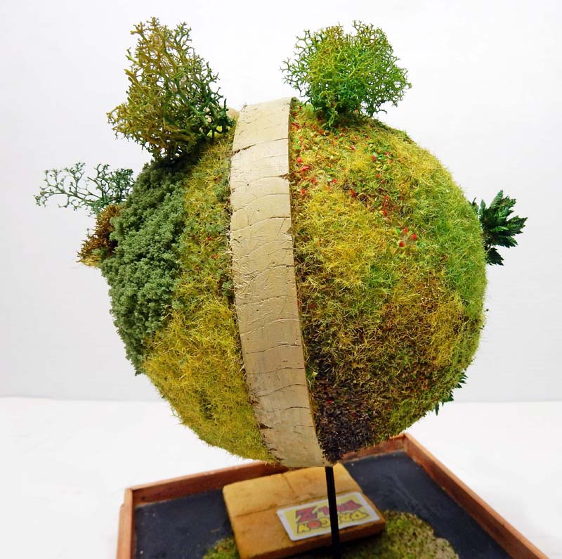 Diorama planète sphérique végétalisée avec route centrale et arbres miniatures, façon Petit Royaume Dragon Ball Z