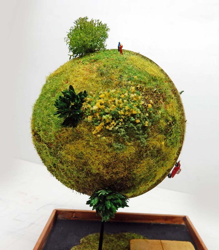 Diorama planète sphérique végétalisée avec arbres et figurine, inspiré de la planète du Maître Kaïo