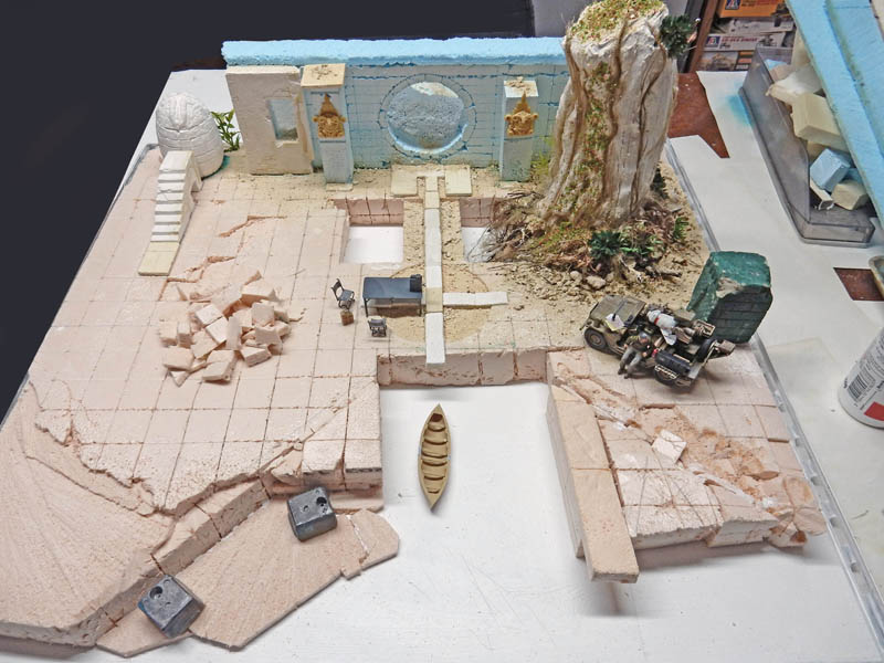 Diorama de maquettisme en construction avec ruines antiques, arbre, camion militaire et barque sur dallage