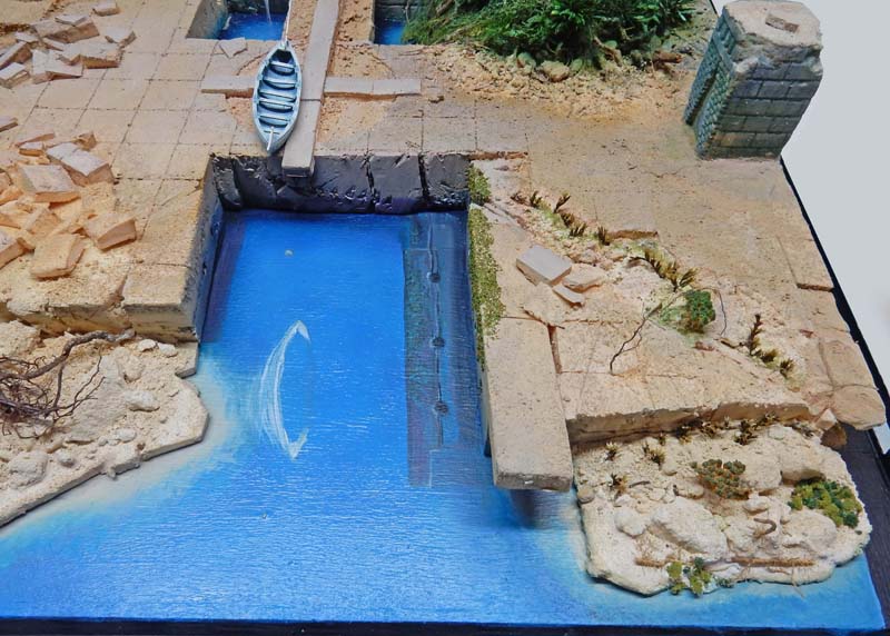Maquette de diorama avec barque et canal d'eau bleue bordé de quais en pierre