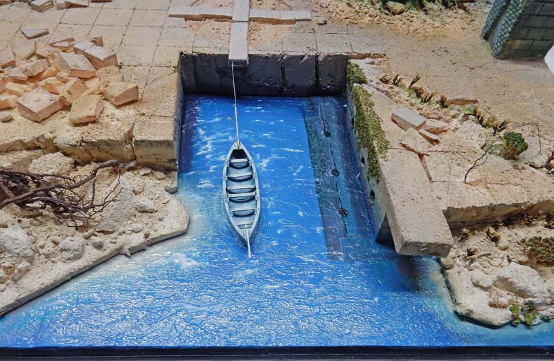 Maquette de bassin portuaire avec petite barque en bois sur eau bleue et quais en pierre