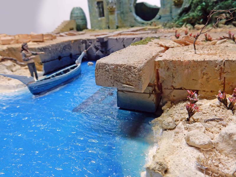 Diorama avec barque et figurine de pêcheur sur un canal bleu bordé de quais en pierre