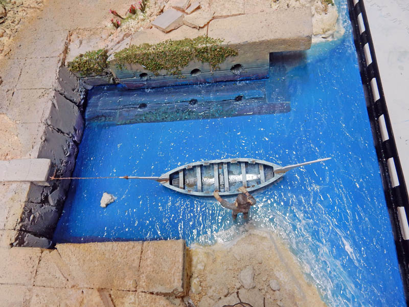 Diorama de maquettisme montrant une barque amarrée sur l'eau bleue près d'un quai en pierre