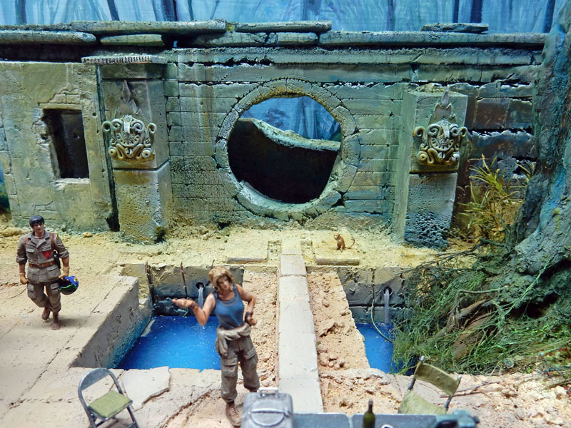 Diorama de maquettisme montrant des figurines près d'un ancien temple en ruine avec bassins