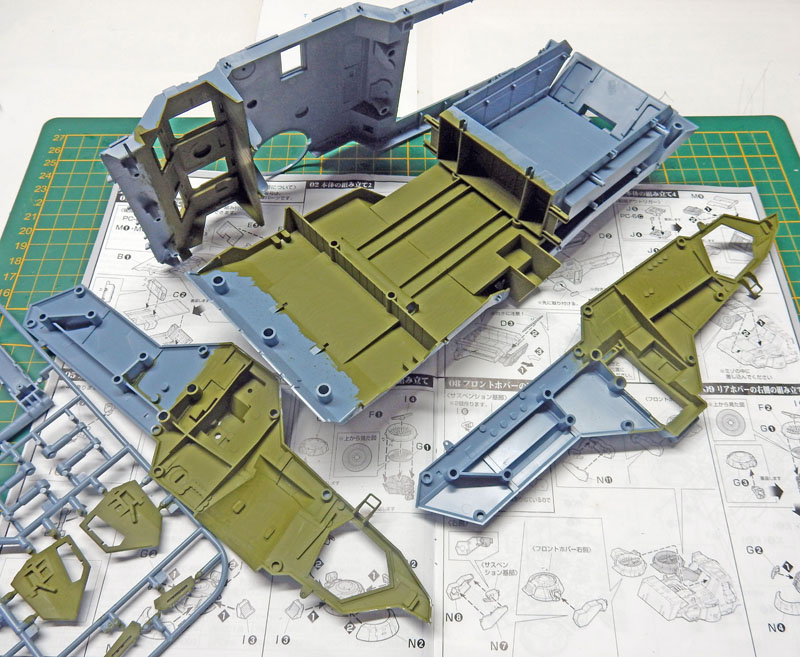 Pièces de maquette peintes en vert et gris posées sur la notice de montage