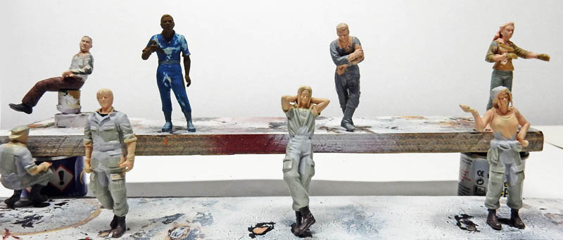 Figurines de personnages peints à différentes étapes alignées sur une planche d'atelier de maquettisme