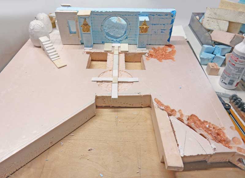 Maquette en construction d'un décor avec mur bleu orné et escalier blanc sur socle rose