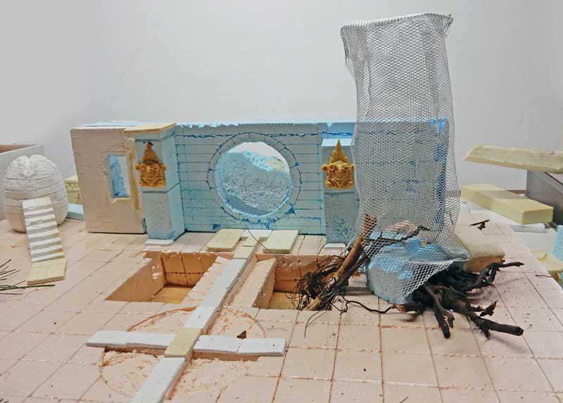 Maquette en construction d'un mur antique avec oculus, racines et grillage formant un arbre