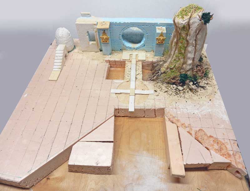 Maquette de cour antique en construction avec mur bleu, arbre et dallage rose