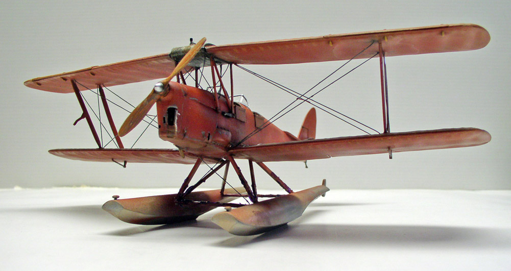 Maquette d'hydravion biplan rouge sur flotteurs, vue de trois quarts sur fond neutre