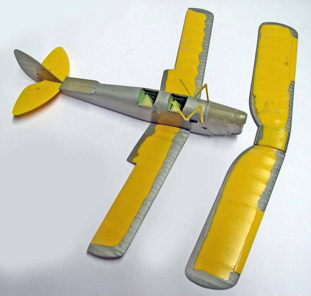 Fuselage et ailes de maquette d'avion en cours d'assemblage, masquage jaune sur apprêt gris