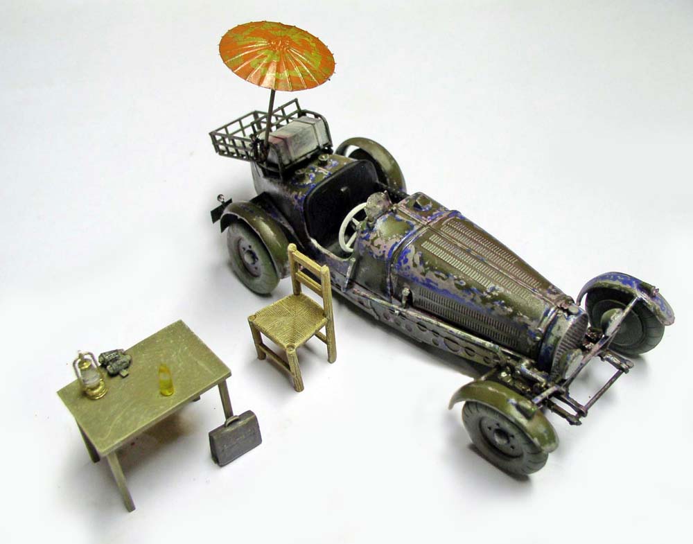 Vieille voiture de course patinée avec ombrelle, table, chaise et lanterne, fond neutre