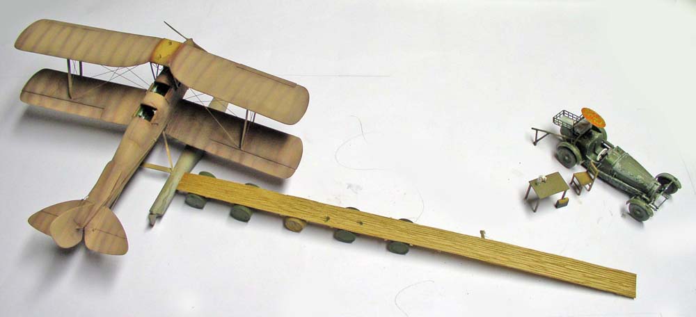 Biplan en toile beige, camion atelier militaire et pièces en attente sur planche de bois