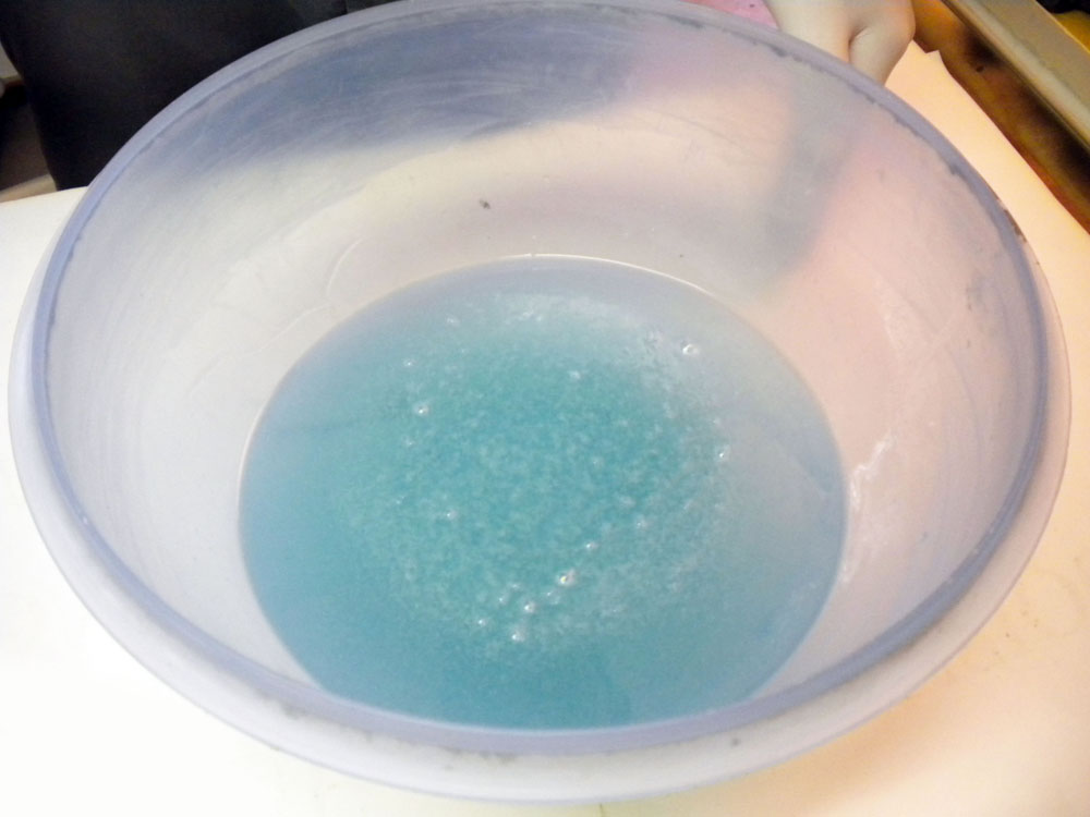 Bassine plastique remplie d'une solution bleutée moussante pour préparation de teinte
