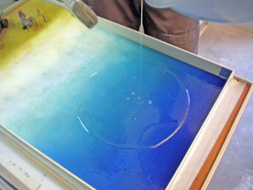 Coulée de résine transparente sur le fond bleu dégradé simulant l'eau du décor