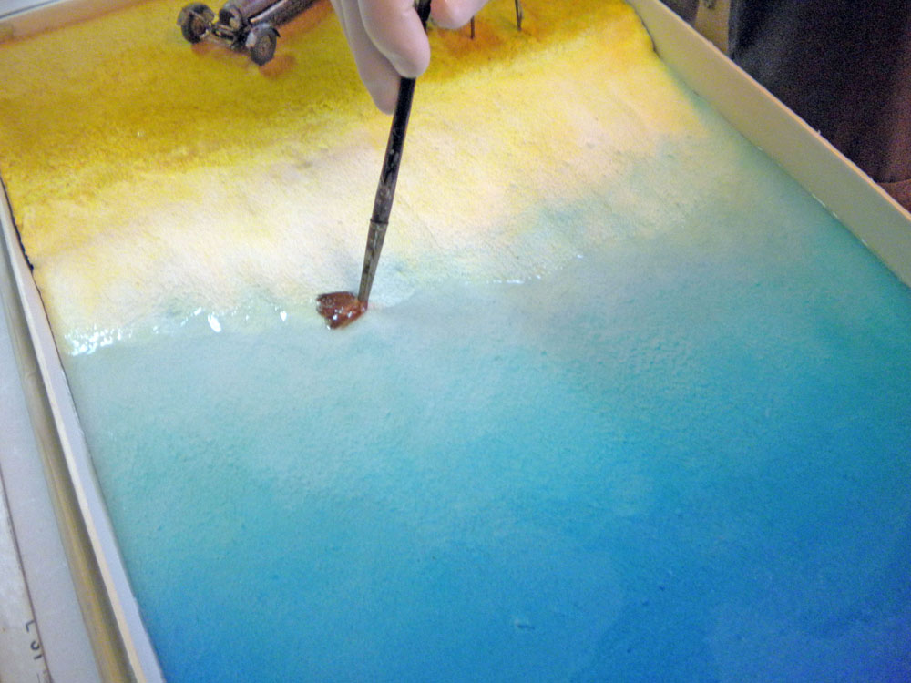 Application au pinceau d'une touche de peinture sur la plage d'un décor marin