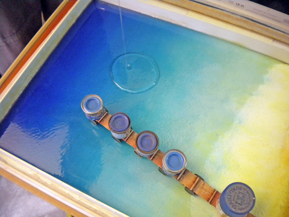 Coulage de résine dans un cadre, dégradé bleu et jaune maintenu par des pots de peinture