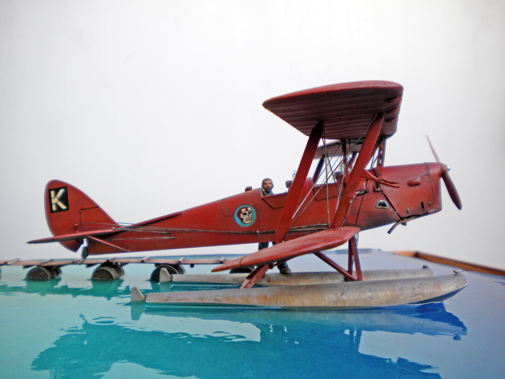 Biplan hydravion rouge à flotteurs posé sur l'eau turquoise, diorama Emile Folks
