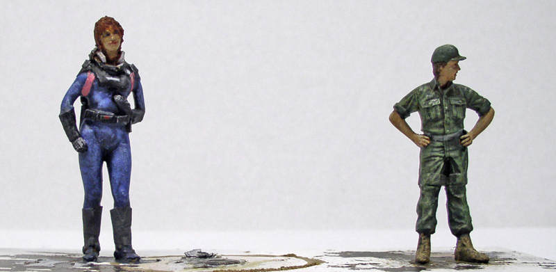 Deux figurines peintes, une femme en combinaison bleue et un soldat en tenue militaire verte