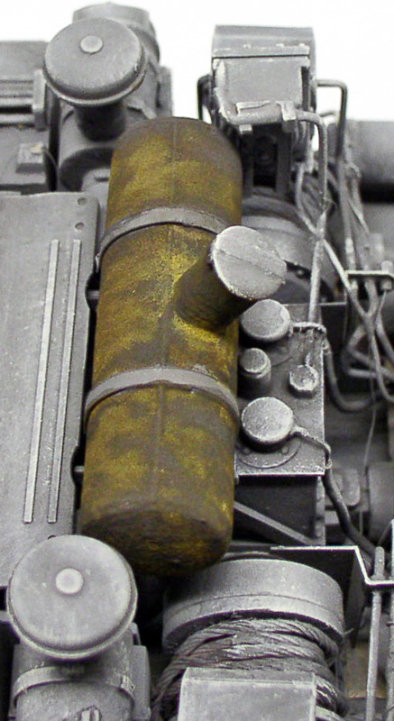 Détail de maquette montrant un réservoir cylindrique rouillé fixé par sangles sur un véhicule gris