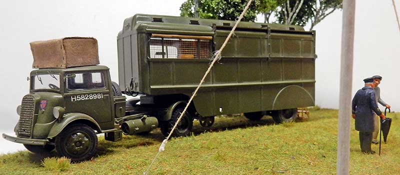 Maquette du tracteur militaire Fordson 7V vert kaki attelé à une remorque, avec figurine dans un diorama