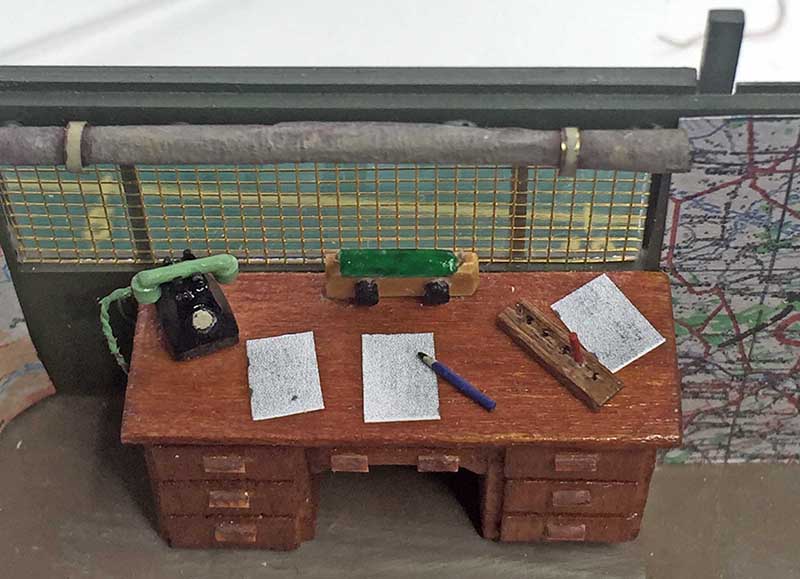 Bureau miniature en bois avec téléphone noir, papiers et stylo devant une carte routière