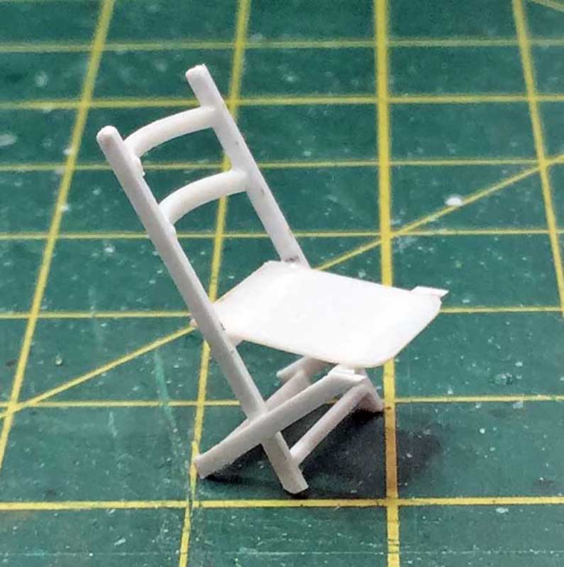 Maquette miniature d'une chaise pliante en plastique blanc posée sur un tapis de découpe vert