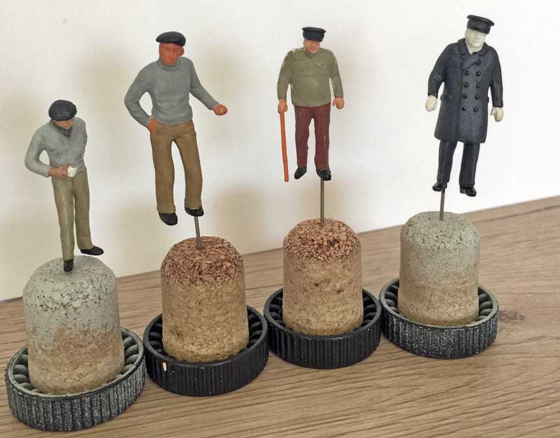 Quatre figurines de personnages peints séchant sur des bouchons de liège pour le diorama
