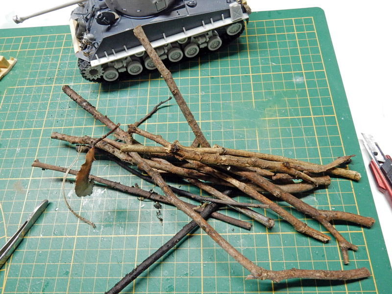 Branches de bois miniatures sur tapis de découpe devant la maquette du char Fury