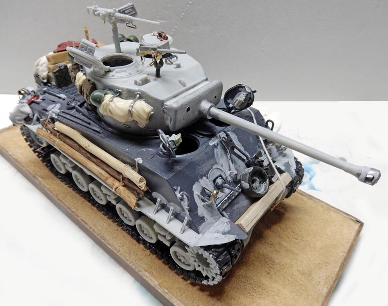 Maquette de char Sherman Fury en cours de peinture grise avec rondins de bois et équipements sur la coque
