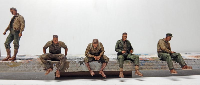 Cinq figurines de soldats américains peintes, quatre assis et un debout sur un socle