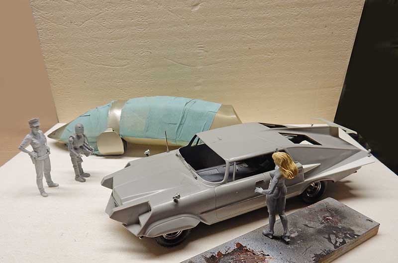 Maquette de voiture futuriste grise en montage avec figurines et fusée masquée à l'arrière-plan