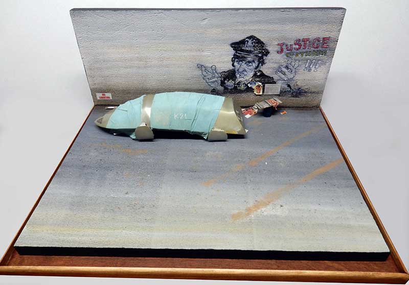 Maquette de pod en cours de masquage sur diorama urbain avec graffiti policier « Justice »