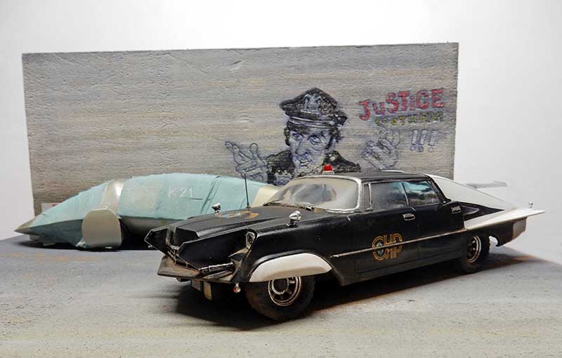 Maquette de voiture de police futuriste noire devant un mur graffé représentant un policier