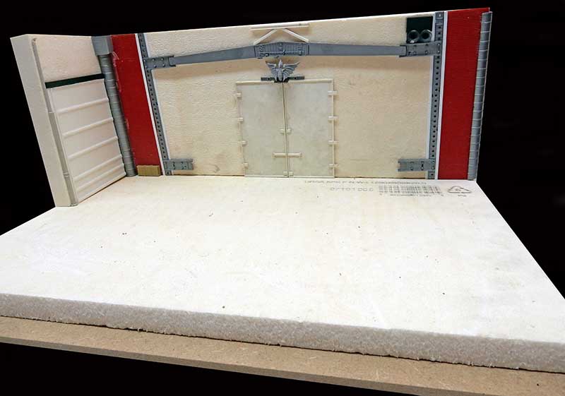 Maquette de diorama en construction montrant un mur intérieur avec porte double et sol blanc