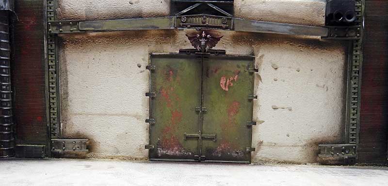 Porte blindée verte vieillie d'un bâtiment en ruine, mur taché et impacts, décor futuriste