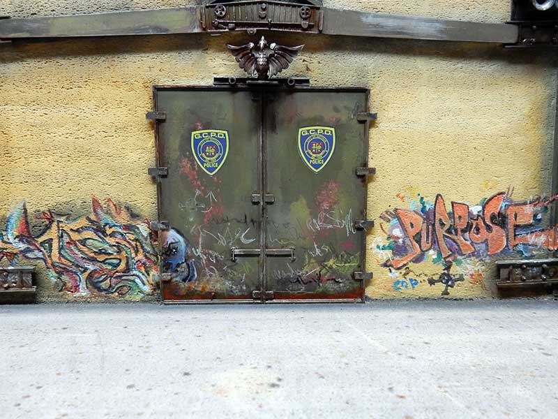 Porte blindée du commissariat GCPD vieillie entourée de graffitis sur mur jaune patiné