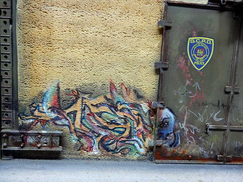 Mur jaune couvert de graffitis colorés à côté d'une porte métallique au logo police G.C.P.D