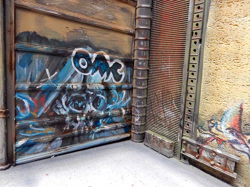 Décor de diorama urbain avec rideau métallique rouillé couvert de graffitis bleus et mur patiné