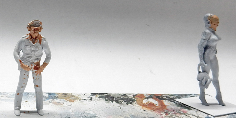 Deux figurines de maquette en cours de peinture, un policier et un personnage gris se faisant face