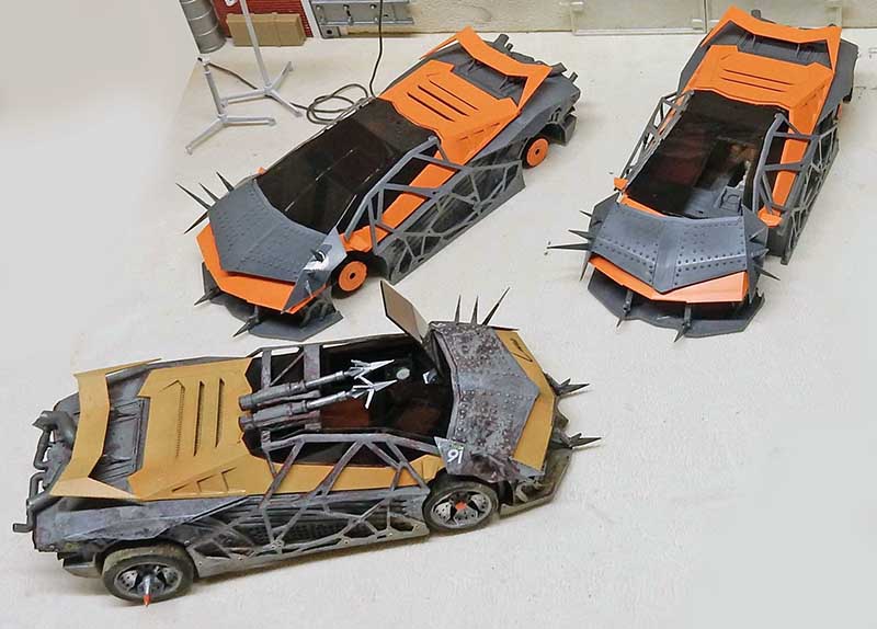 Trois maquettes de voitures de combat blindées à pointes, orange et grises, du film Future Cop