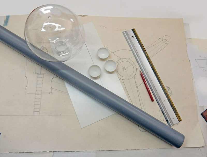 Sphère et demi-sphères transparentes, tube gris et règle posés sur des plans de maquette