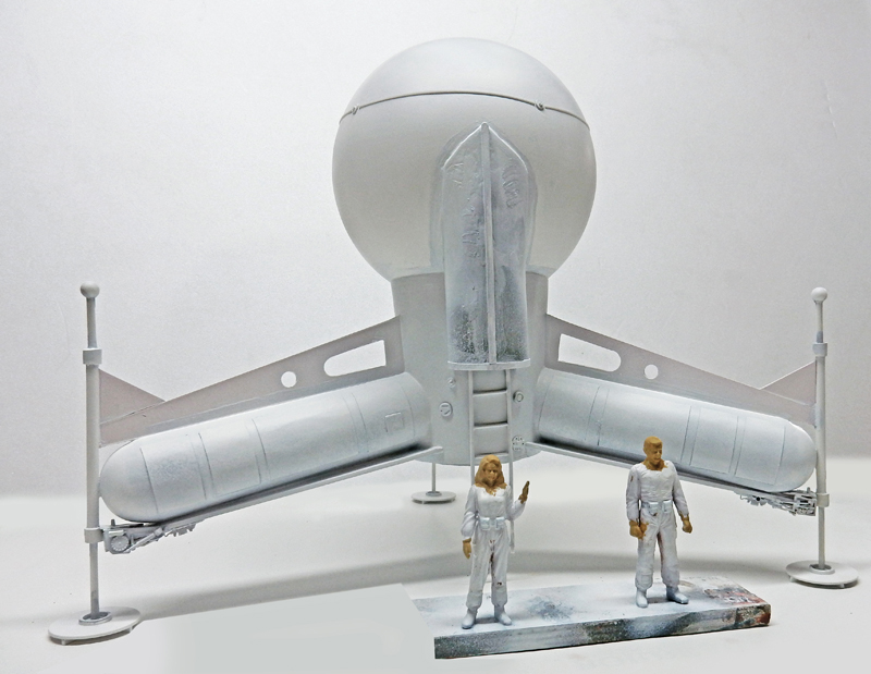 Maquette blanche du vaisseau G.N.U. avec sphère et deux figurines de pionniers en combinaison devant
