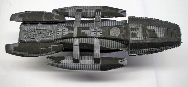 Maquette du vaisseau Battlestar Galactica vue de dessus, coque grise détaillée sur fond blanc