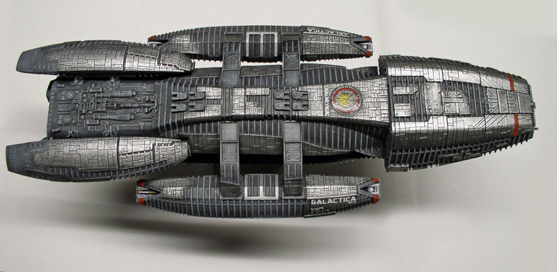 Maquette du cuirassé Battlestar Galactica vue de dessus, coque grise détaillée sur fond clair