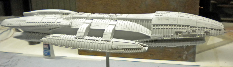 Maquette du Battlestar Galactica en apprêt gris posée sur un support de travail